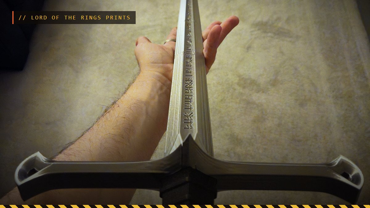 A hand holding a 3D printed Narsil sword hilt in silver, by Sam